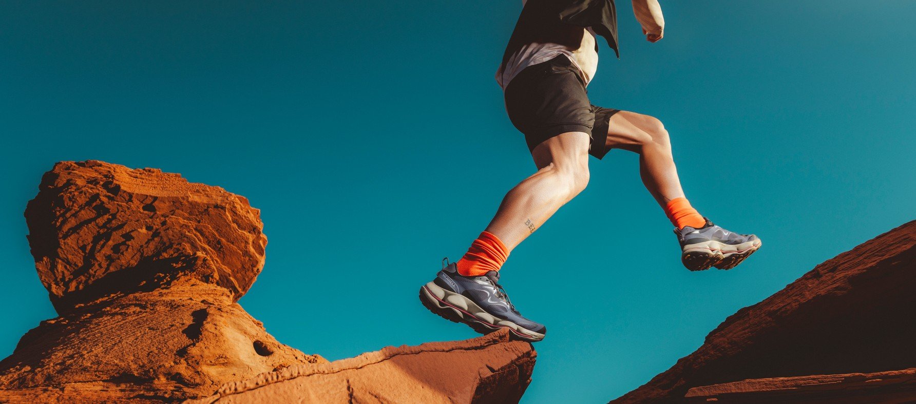 Runner leaping between red desert rocks in Merrell SpeedARC shoes